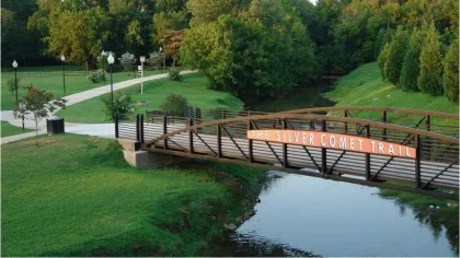 Footbridge over a creek on The Silver Comet Trail surrounded by greenery and walking paths under clear skies.