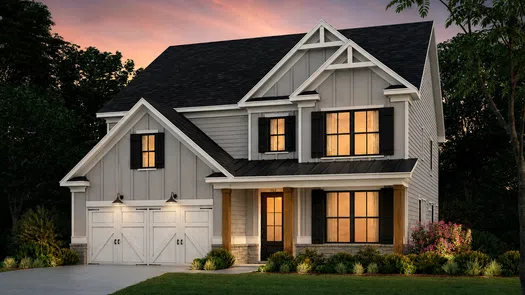 Modern two-story gray house with black shutters, warm interior lights, and a landscaped front yard at sunset