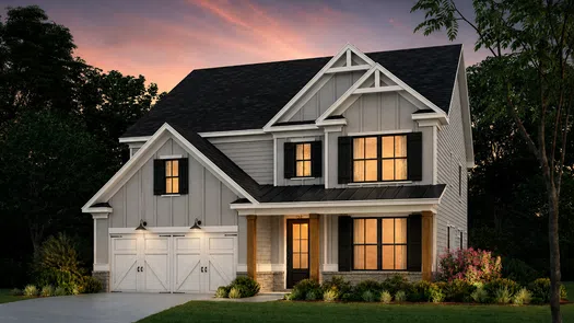 Modern two-story gray house with black shutters, warm interior lights, and a landscaped front yard at sunset